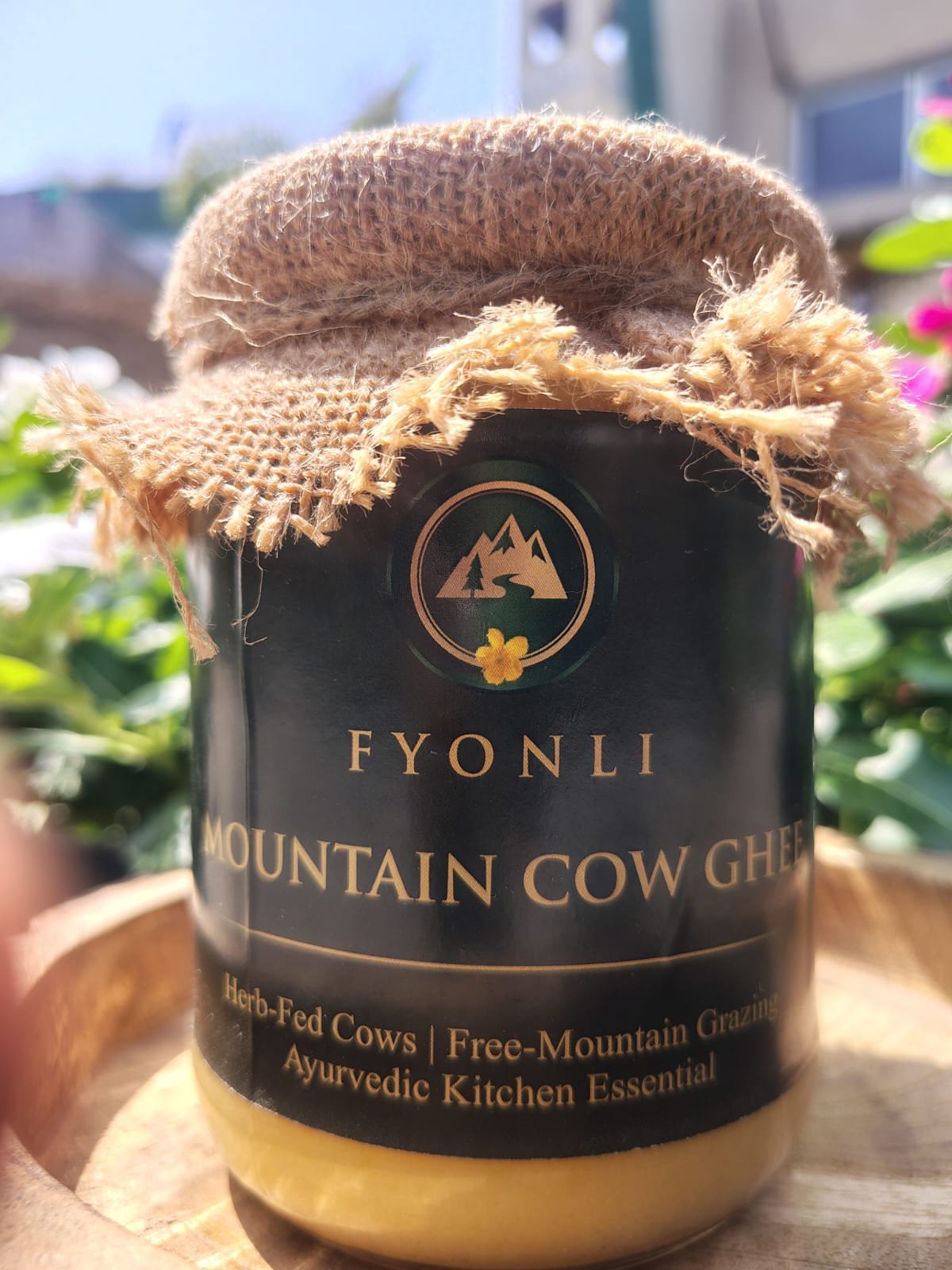 Fyonli Mountain Cow Ghee 400g on wooden platform – garden background